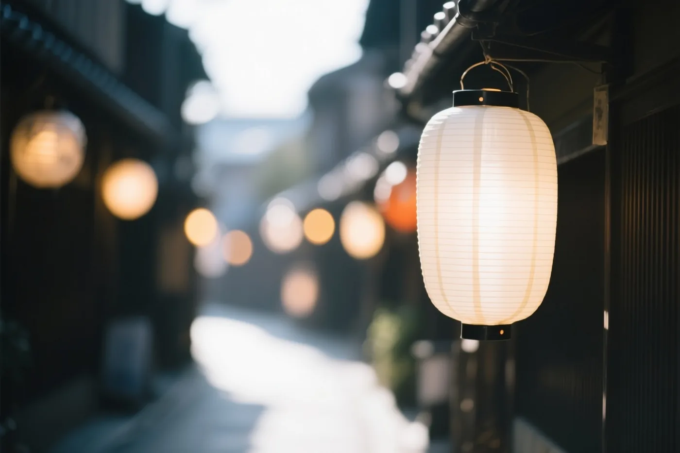 Een warm verlichte papieren lampion hangt scherp in beeld in een donker steegje met traditionele gebouwen en onscherpe ronde lichtjes op de achtergrond.