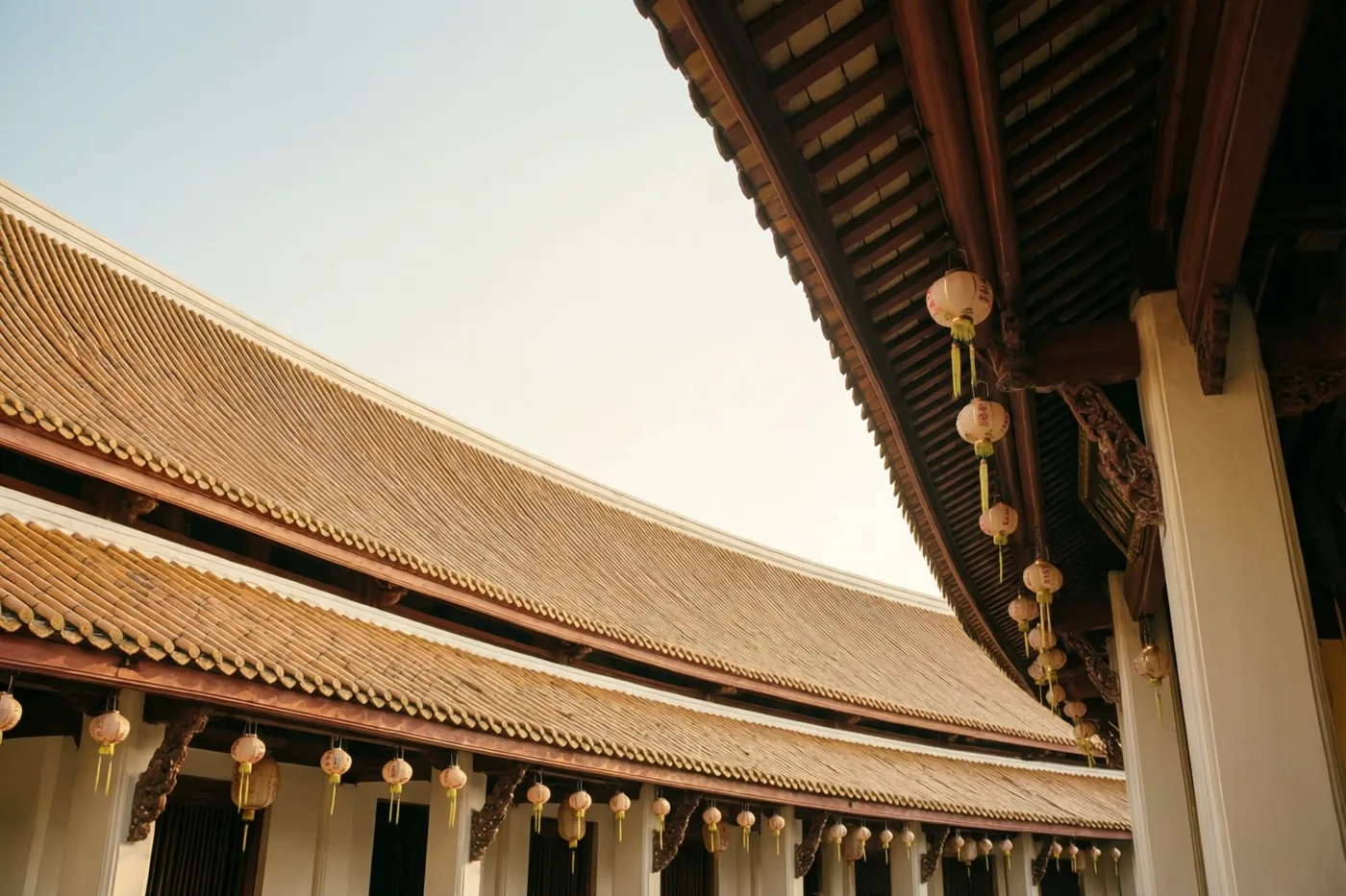 Een laag standpunt toont de gebogen pannendakranden van een traditionele tempel met hangende papieren lantaarns in bruine, beige en lichtblauwe tinten.