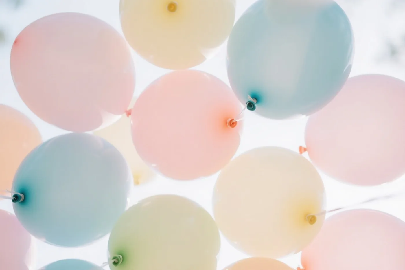 Een tros zachtroze, lichtblauwe en crèmekleurige ballonnen vult van onderaf gezien het beeld tegen een helderwitte achtergrond.