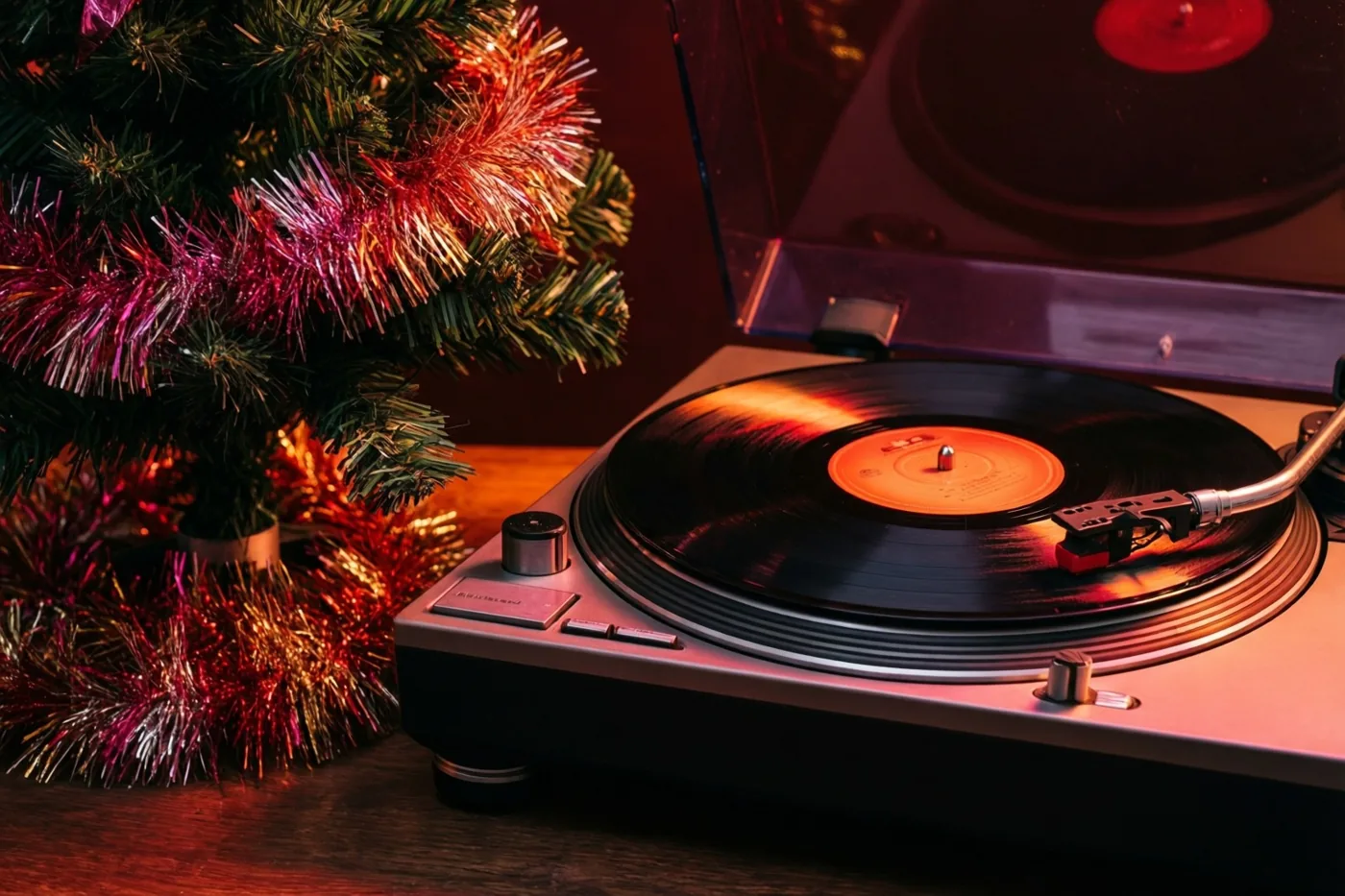 Een vinylplaat draait op een platenspeler naast een kerstboom met rode en gouden glitterslingers in warm rood licht.