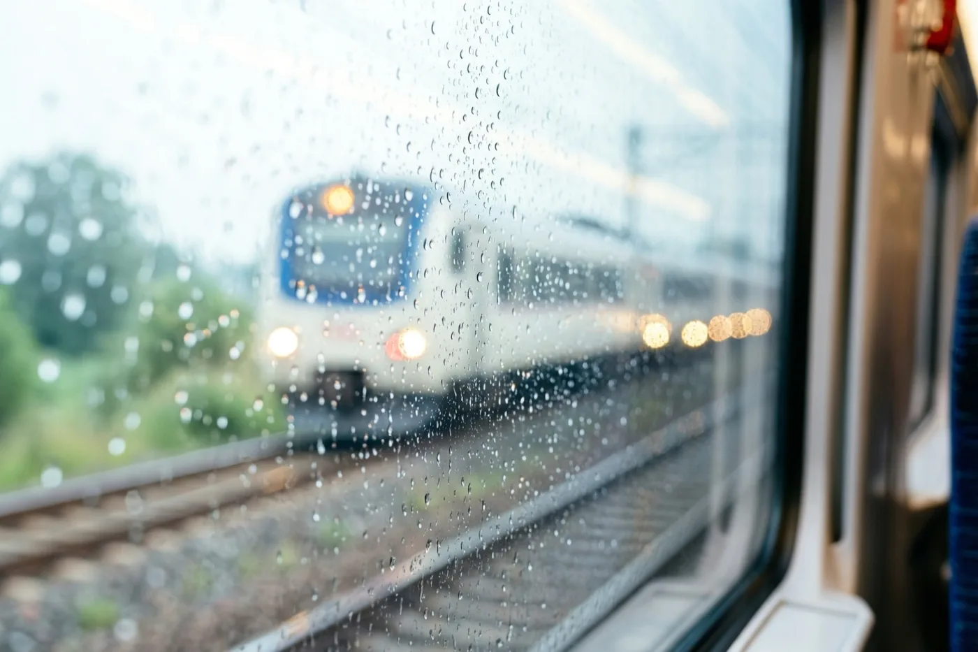 Regendruppels op een treinraam vervagen het zicht op een andere trein en zijn warme gele lichten op de sporen ernaast.