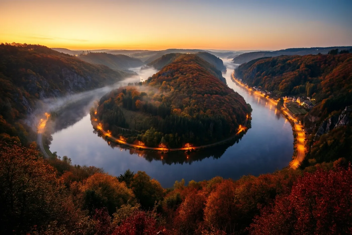 Een kronkelende rivier stroomt tussen beboste heuvels in herfstkleuren, omringd door ochtendmist en gouden licht van de opkomende zon.