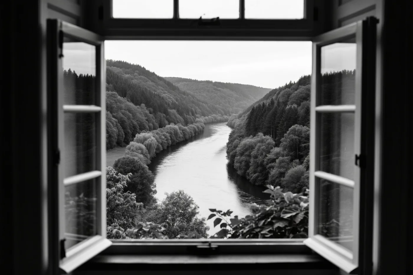 Een zwart-witfoto toont door een open raam een kronkelende rivier tussen beboste heuvels.
