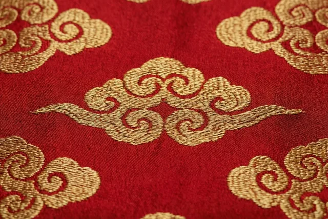 Een detailopname toont dieprode zijde met een fijn ingeweven gouden wolkenpatroon.
