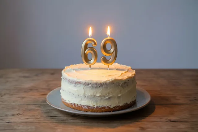 Een zelfgemaakte roomtaart met brandende cijferkaarsjes die 69 vormen staat op een houten tafel in warm kaarslicht.
