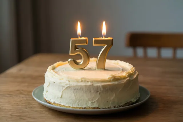 Een zelfgemaakte roomtaart met brandende cijferkaarsjes 57 staat op een houten tafel in warm kaarslicht.