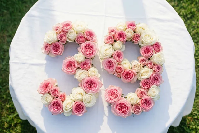Van bovenaf zijn roze en witte rozen te zien die 39 vormen op een wit tafelkleed buiten op het gras.