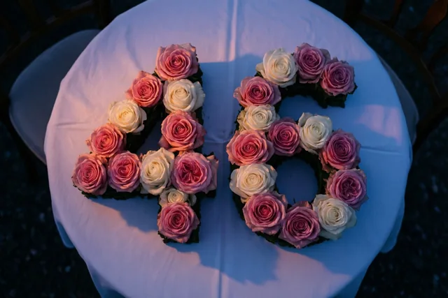 Roze en witte rozen vormen het getal 46 op een wit tafelkleed, recht van boven gezien in zacht licht.