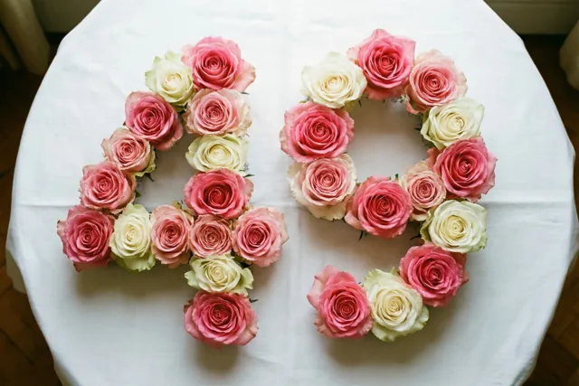 Roze en witte rozen vormen 49 op een wit tafelkleed, recht van boven gefotografeerd.