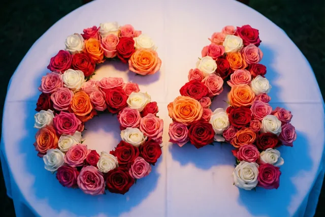 Roze en witte rozen vormen het getal 64 op een wit tafellaken, van bovenaf gefotografeerd in helder licht.
