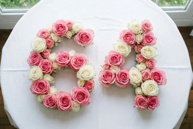 Roze en witte rozen vormen het getal 64 op een wit tafellaken, van bovenaf gezien met natuurlijk licht uit ramen op de achtergrond.