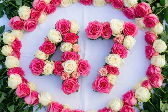 Roze en witte rozen vormen een symmetrisch geschikt getal 47 op een wit tafelkleed, van bovenaf gezien met groene stelen rondom.
