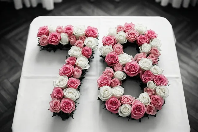 Van bovenaf is 78 van roze en witte rozen op een wit tafellaken te zien, met een donkere houten vloer op de achtergrond.