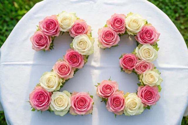 Roze en witte rozen vormen 23 op een wit tafelkleed buiten, van bovenaf gezien met groen gras op de achtergrond.