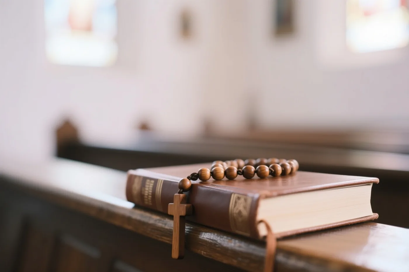 Een houten rozenkrans met kruis ligt op een gesloten leren gebedenboek op een houten kerkbank.