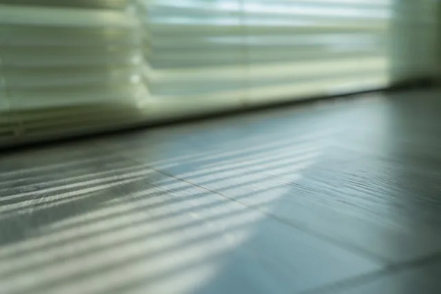 Zacht daglicht valt door horizontale jaloezieën en werpt gestreepte schaduwen op een houten vloer.