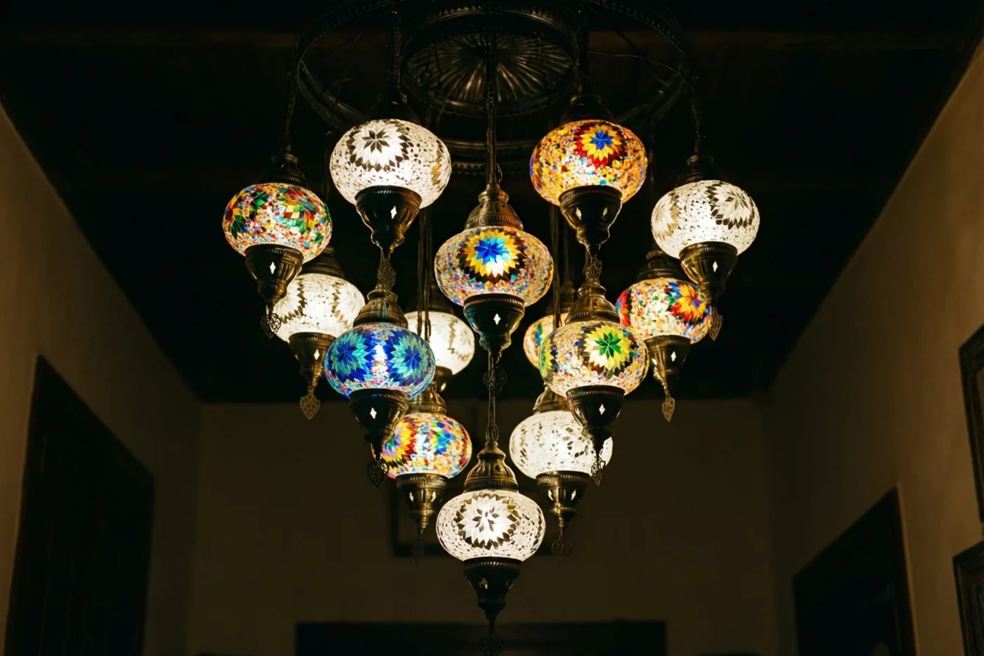 Sierlijke Marokkaanse glazen lantaarns met patronen in diepe kleuren hangen aan een donker plafond en geven warm licht in een schemerige kamer.