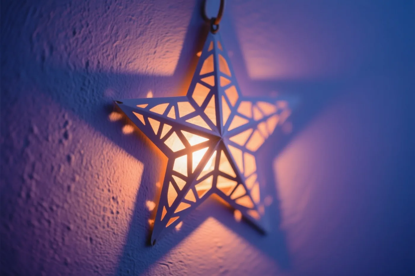 Een hangende sterlantaarn met een geometrisch uitgesneden patroon werpt warm licht op een muur met structuur in een blauwpaarse omgeving.