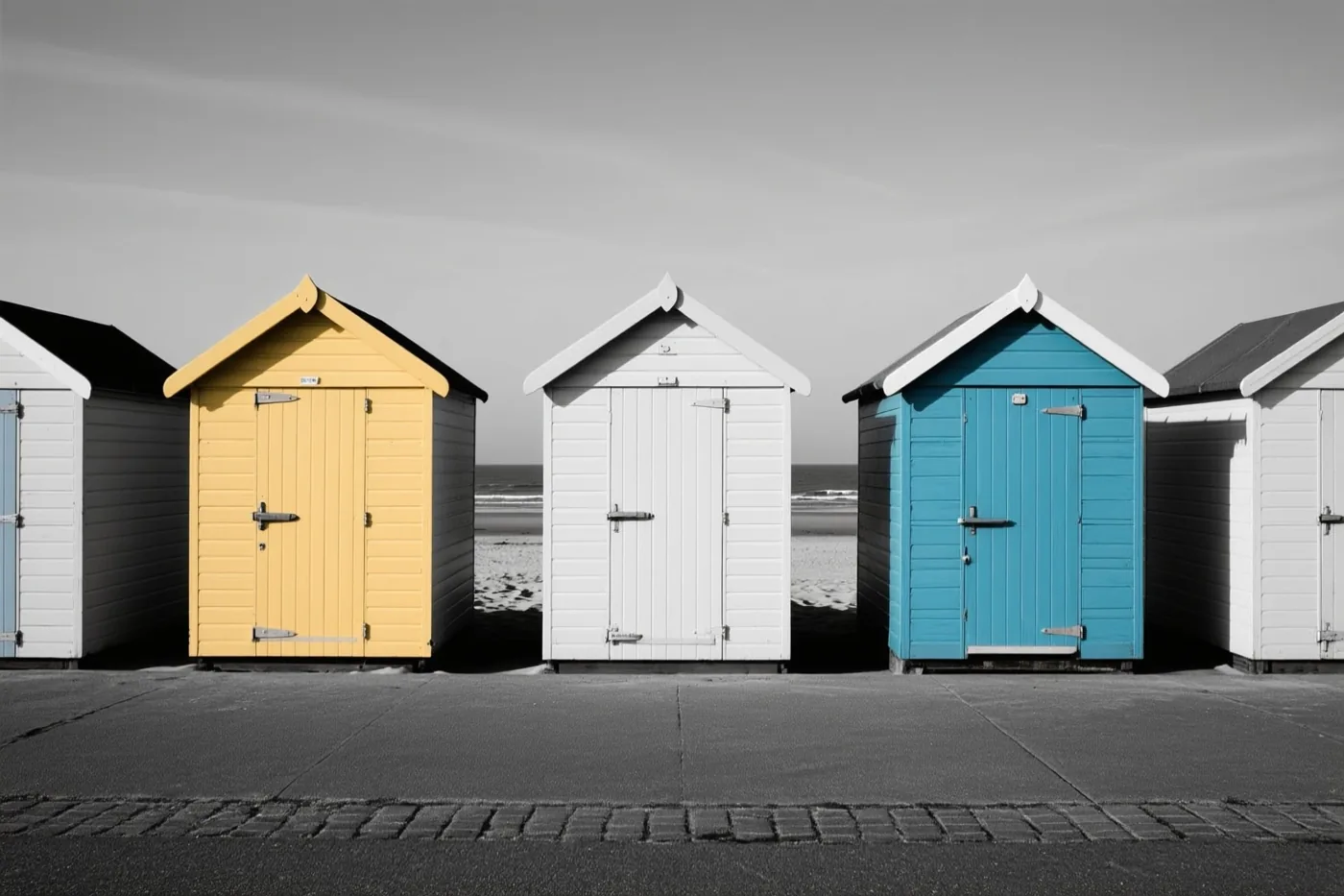 Gele, witte en blauwe strandhuisjes staan op een verharde promenade met de zee op de achtergrond.