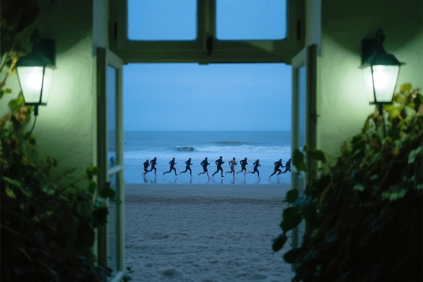 Door een open deuropening met brandende wandlampen aan weerszijden is een groep mensen te zien die in blauwgroene schemering over het strand naar zee rent.