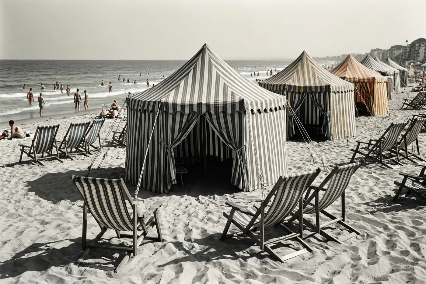 Gestreepte strandtenten en houten ligstoelen staan op een zandstrand met badgasten bij de zee in de verte, in warme vervaagde kleuren.