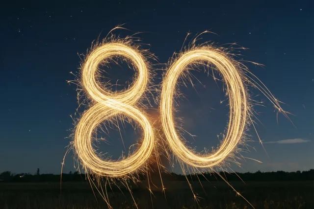 Gouden lichtsporen van sterretjes vormen 80 onder een diepblauwe sterrenhemel boven een open veld met een verre bomenrij.