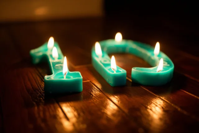 Brandende theelichtjes vormen het getal 10 op een donkere houten vloer in blauwgroene en amberkleurige tinten.