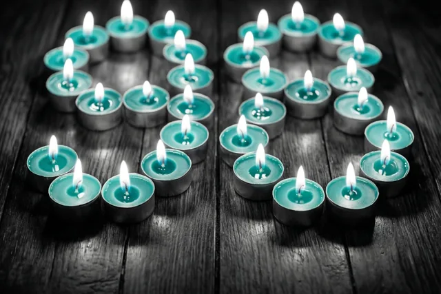 Brandende theelichtjes vormen 98 op een donkere houten vloer in een beeld met vooral blauwgroene en zwarte tinten.