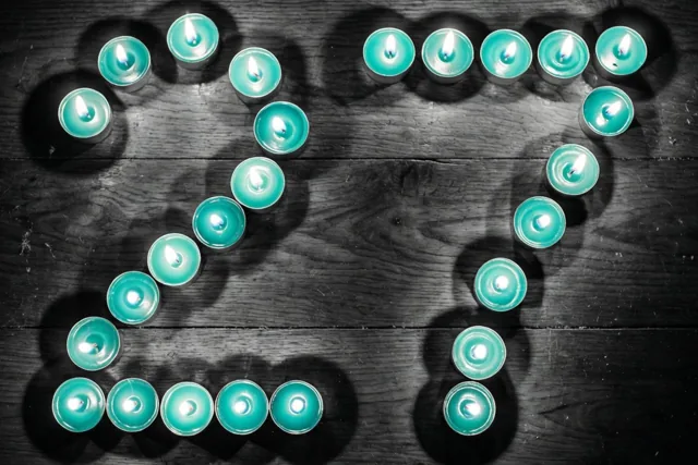 Brandende theelichtjes vormen het getal 27 op een donkere houten vloer in een beeld met blauwgroene en zwarte tinten.