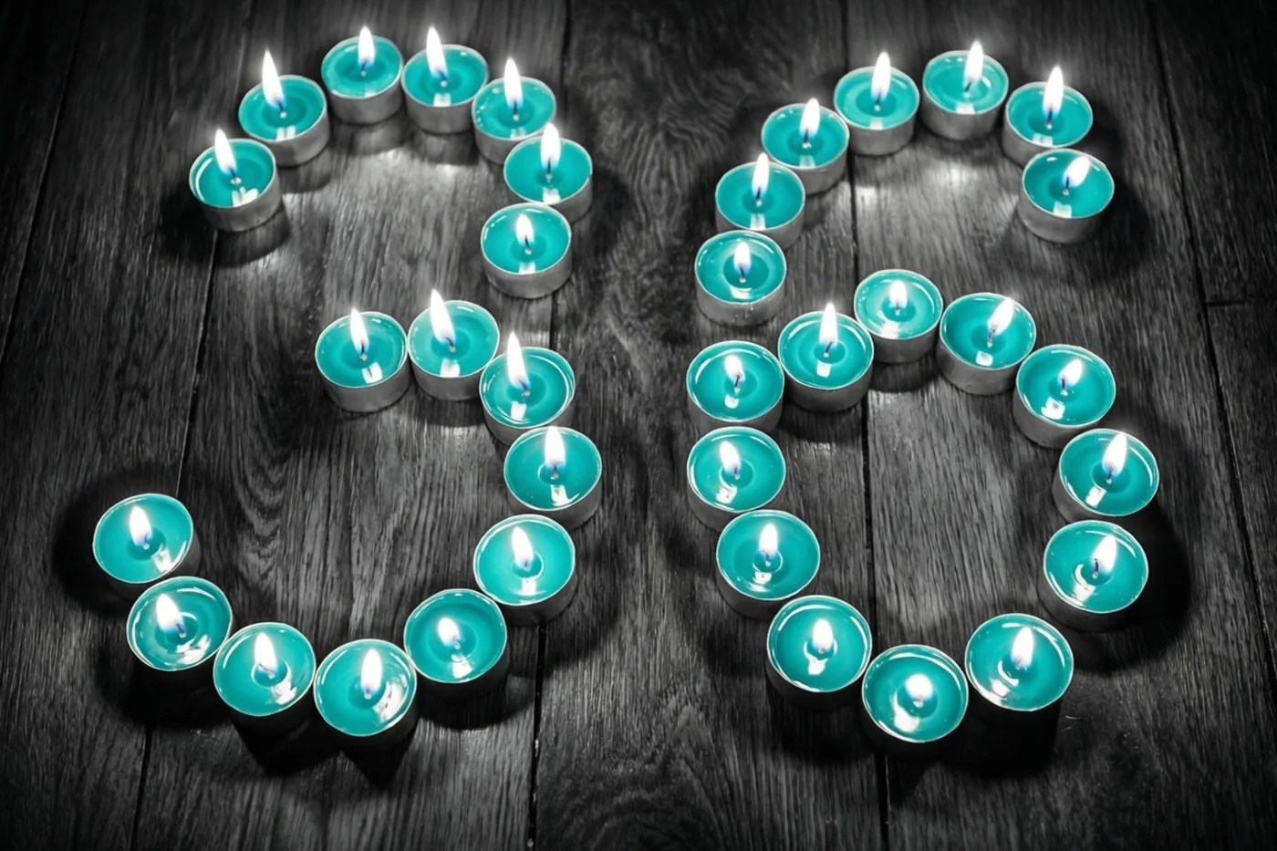 Brandende theelichtjes vormen het getal 36 op een donkere houten vloer, met blauwgroene en zwarte tinten rond het warme kaarslicht.
