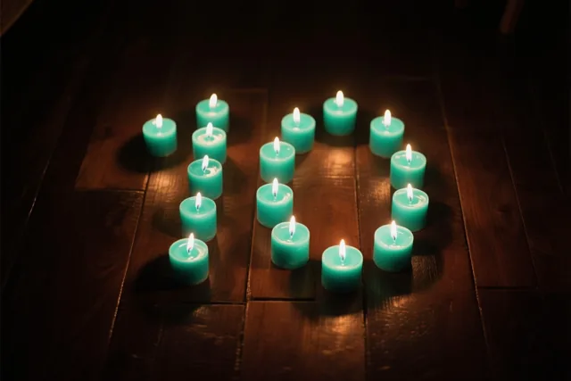 Brandende theelichtjes vormen het getal 10 op een donkere houten vloer en verspreiden een warme gloed.