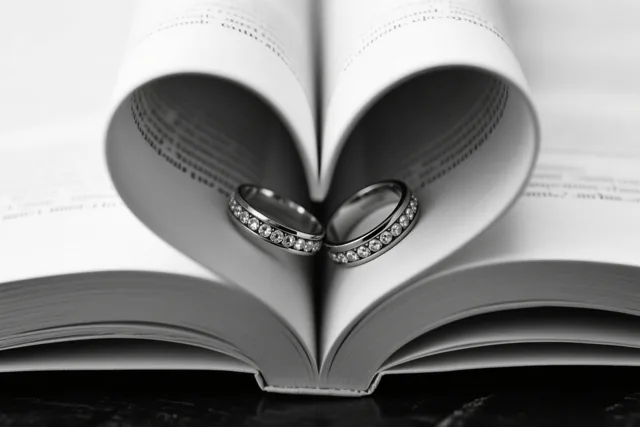Een zwart-witfoto toont twee trouwringen met diamanten in een open boek waarvan de gebogen bladzijden een hart vormen.