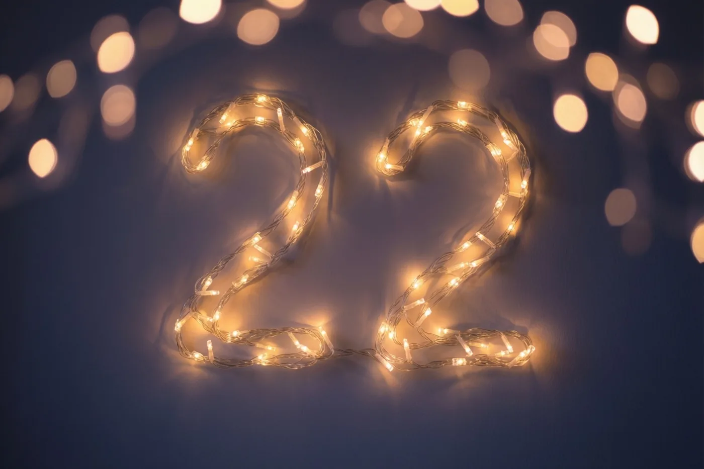 Warme lichtjes vormen 22 op een donkere muur, met onscherpe feestlichtjes op de achtergrond.