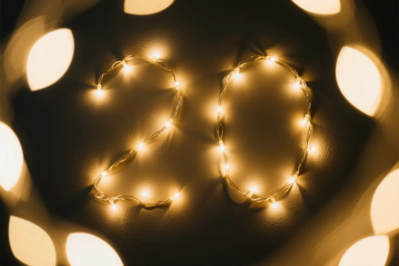 Het getal 20 van warme lichtslingers hangt op een donkere muur met structuur, met onscherpe feestlichtjes op de achtergrond.