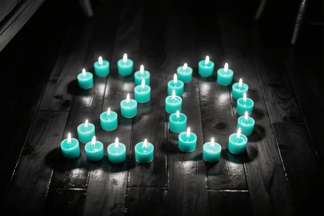 Brandende theelichtjes staan in de vorm van 20 op een donkere houten vloer, met een warme gloed tussen blauwgroene en zwarte tinten.