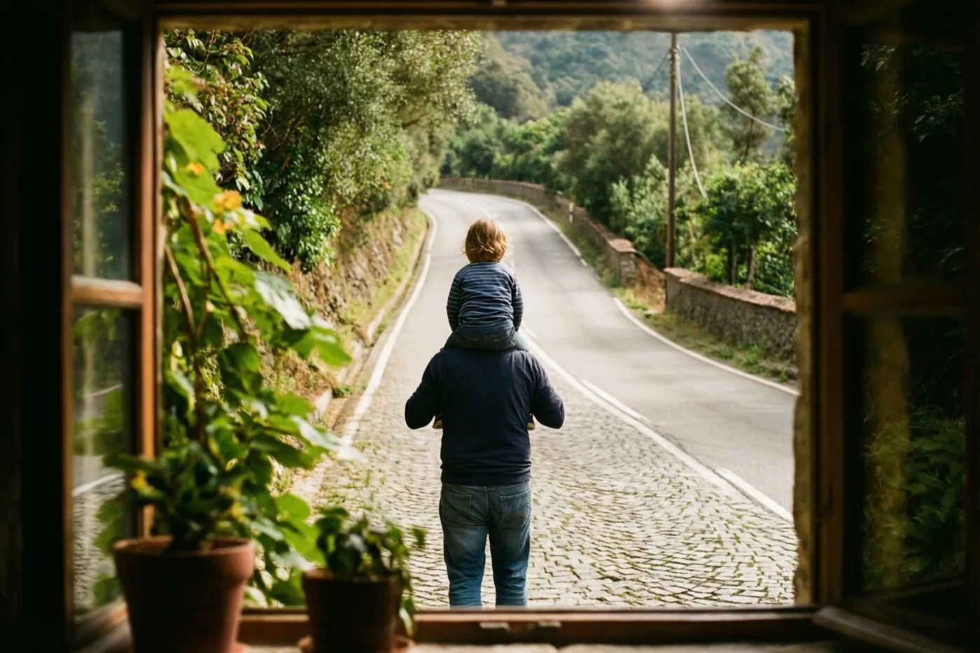 Door een raam met een houten kader is een vader van achteren te zien die een kind op zijn schouders draagt over een kronkelende kasseiweg in een groen heuvellandschap.