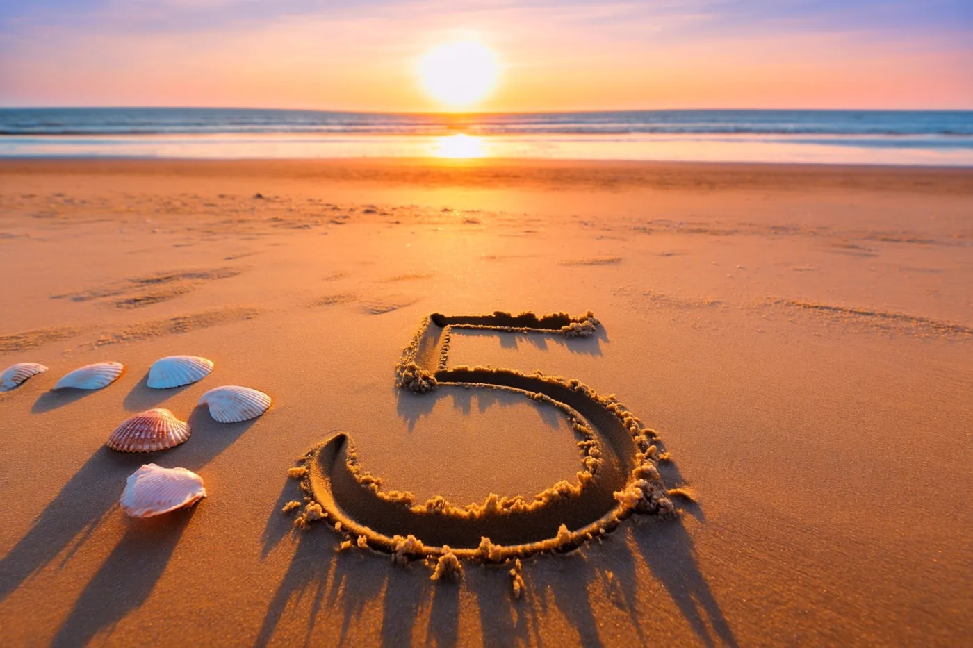 Het cijfer 5 is in het strandzand getekend met enkele schelpen ernaast, in het oranje en roze licht van de ondergaande zon boven zee.