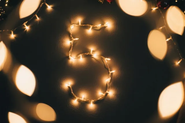 Warme lichtjes vormen het cijfer 5 op een donkere muur, met warme gele en donkerbruine tinten.