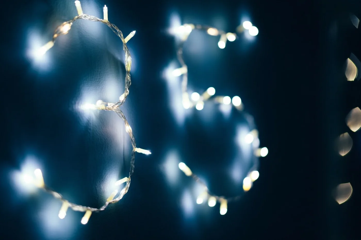 Warme lichtjes vormen 35 tegen een donkere muur, met wazige lichtpunten en een koele blauwe tint op de achtergrond.