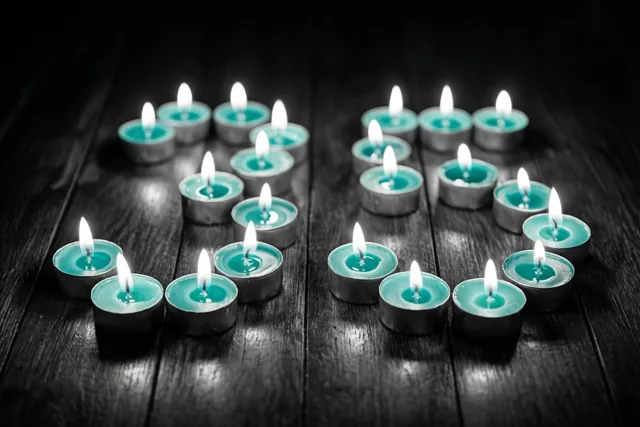 Brandende blauwgroene theelichtjes vormen 35 op een donkere houten vloer in een verder monochroom beeld.