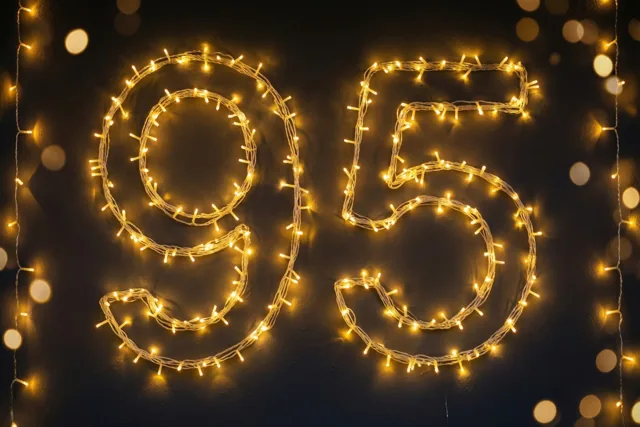 Het getal 95 is gevormd met warm gloeiende lichtjes op een donkere muur, met onscherpe lichtjes op de achtergrond.