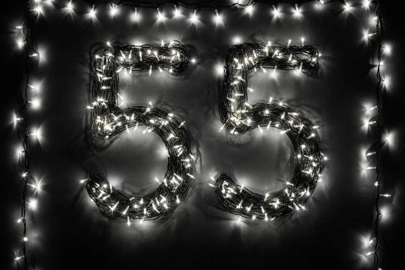 Lichtjes vormen het getal 55 op een donkere muur, met wazige lichtvlekken en extra lichtslingers langs de randen.