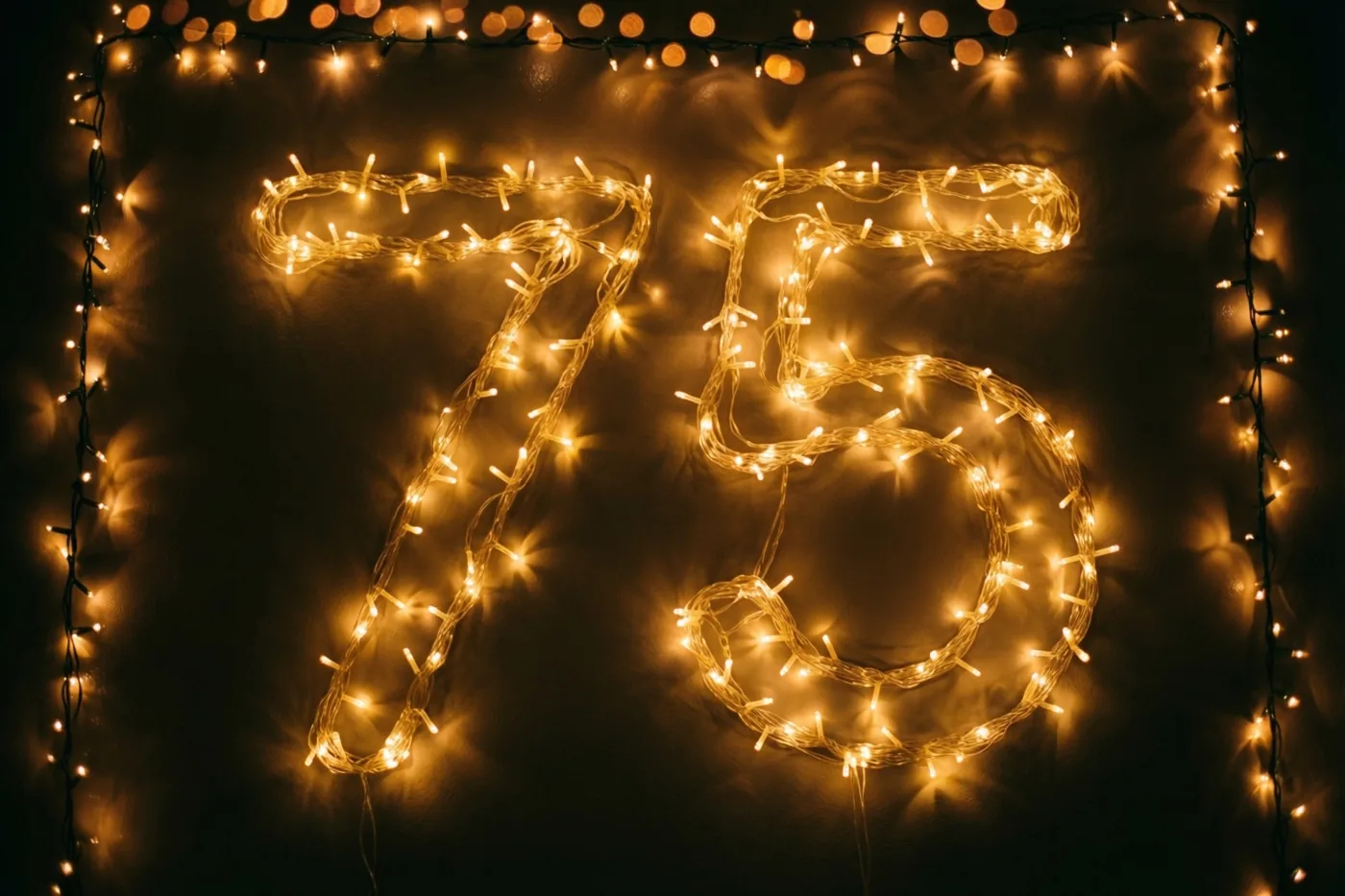 Warme lichtjes vormen 75 op een donkere muur, omlijst door extra lichtslingers die wazig in beeld komen.