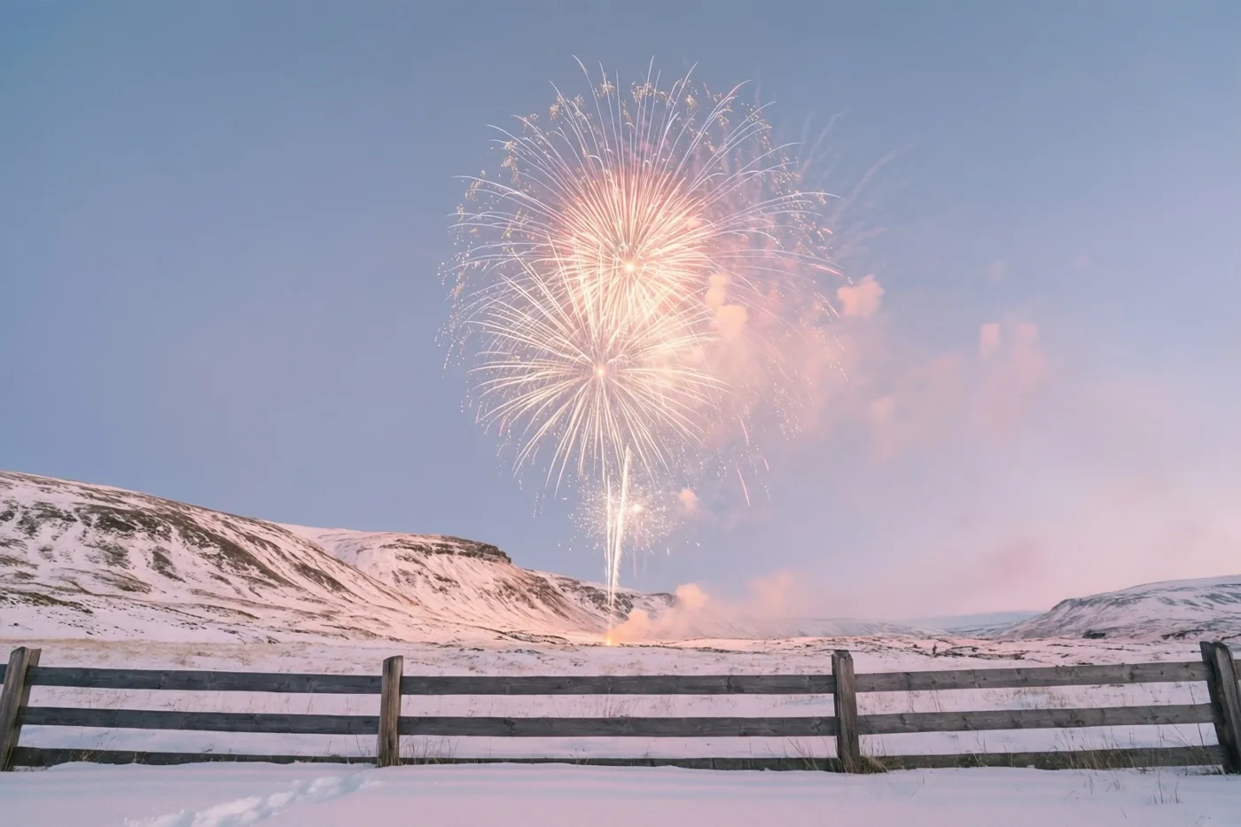 Een grote vuurwerkuitbarsting verlicht besneeuwde heuvels in koele blauwe en roze tinten, met een verweerde houten omheining op de voorgrond.