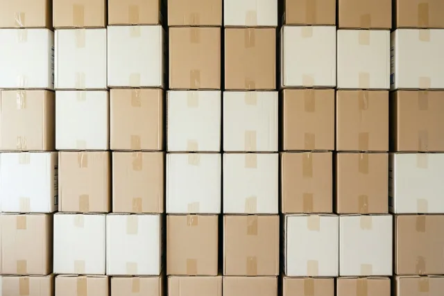 Een wand van netjes gestapelde kartonnen verhuisdozen vormt een herhalend patroon in beige en wit.