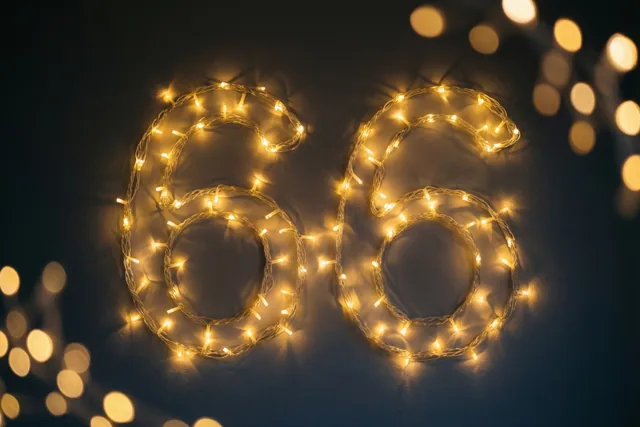 Warme lichtslingers vormen het getal 66 op een donkere muur, met onscherpe lichtjes op de achtergrond.
