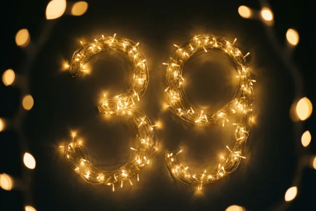 Warme lichtslingers vormen 39 tegen een donkere muur met onscherpe feestlichtjes op de achtergrond.