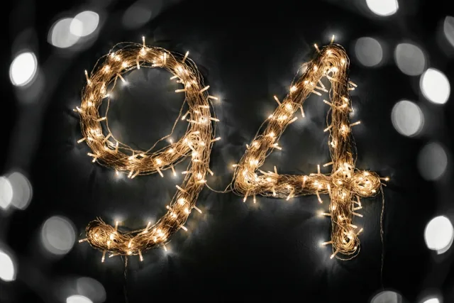 Warme lichtjes vormen 94 tegen een donkere muur, met onscherpe feestlichtjes op de achtergrond.