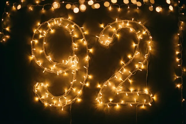 Warmgele lichtjes vormen 92 tegen een zwarte muur, met zachte onscherpe lichtpunten op de achtergrond.