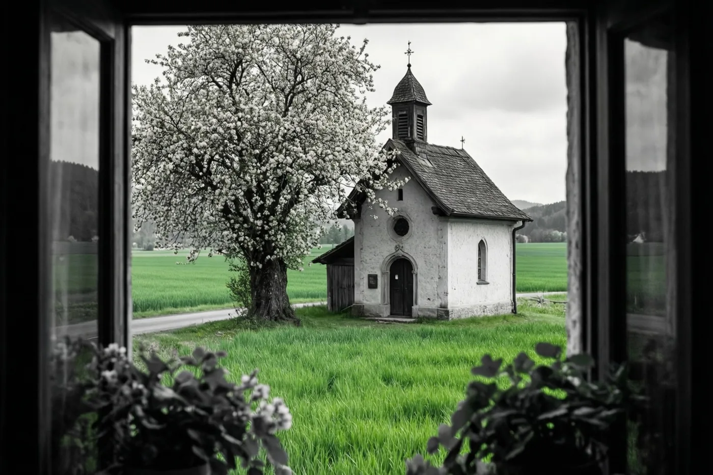 Door een raam zie je een witte kapel met donker dak en klokkentoren naast een witbloeiende boom, tussen groene velden onder een bewolkte hemel.
